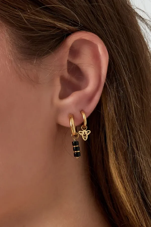 Gouden oorbellen met bij-bedeltje en zwarte steentjes.