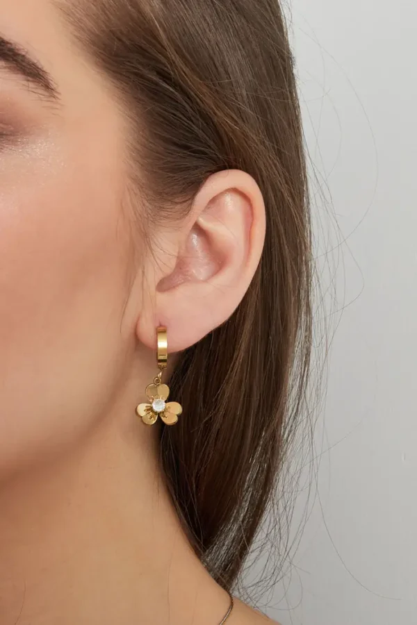 Vrouw draagt gouden bloemvormige oorbel.