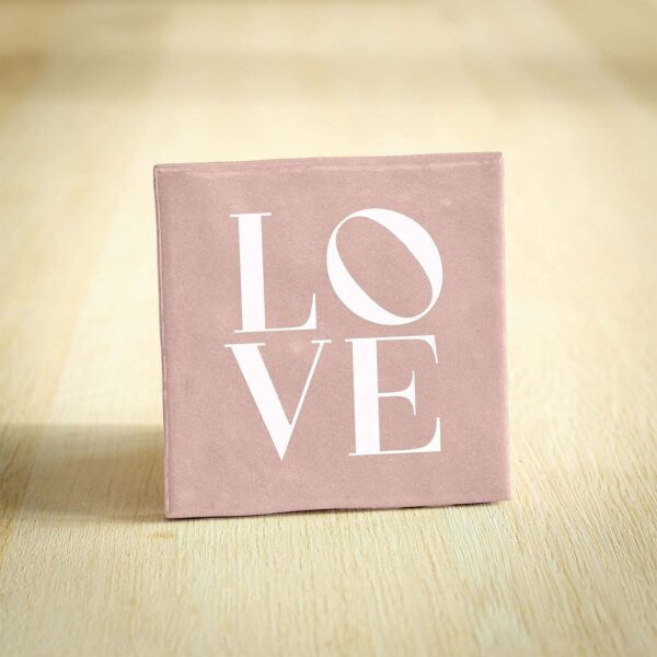Roze tegel met "LOVE" tekst op houten ondergrond.
