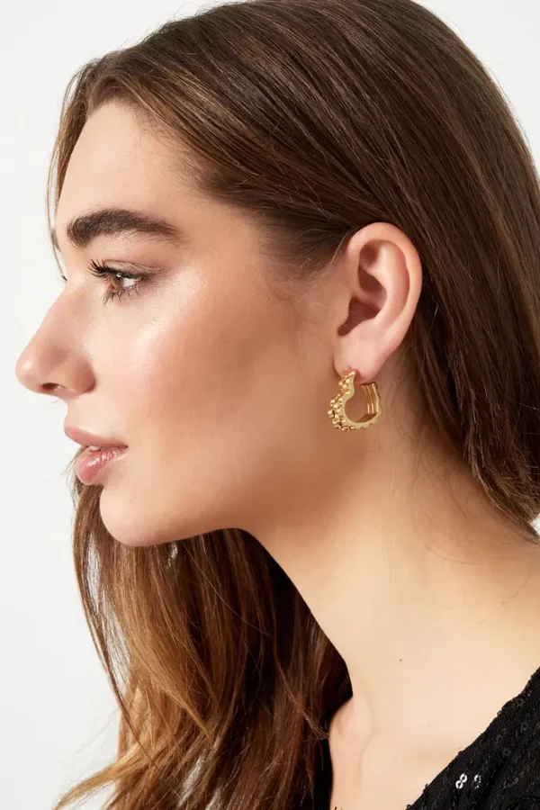 Vrouw draagt gouden oorring met uniek ontwerp.